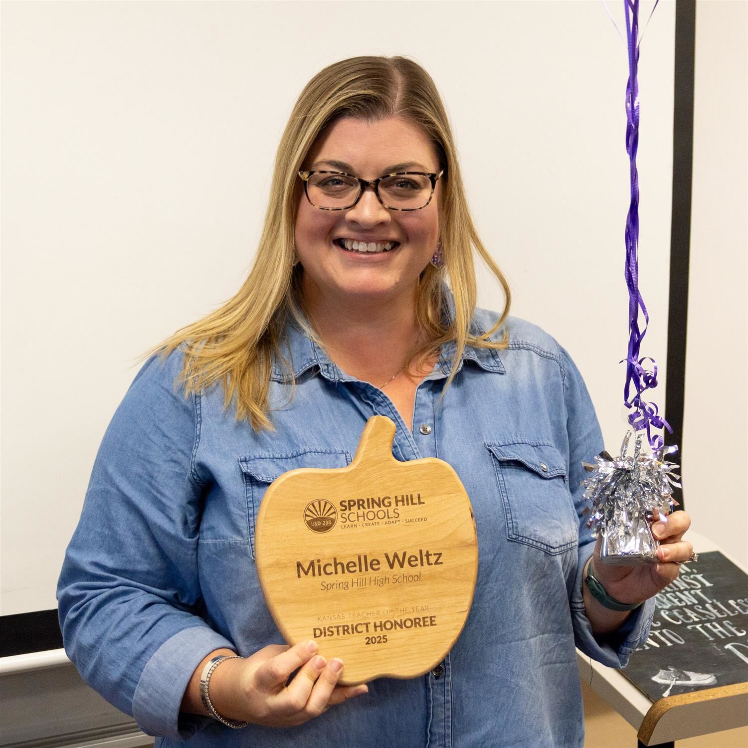 Michelle Weltz holding wooden, apple-shaped Teacher of the Year award plaque and balloons