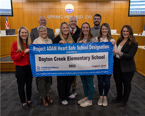 DCES building team smiling in a group with Project ADAM banner