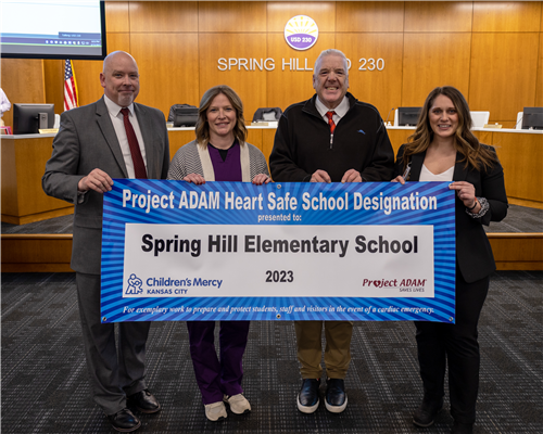 SHES building team smiling in a group with Project ADAM banner