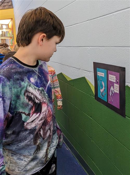Student reading book page hanging on hallway wall.