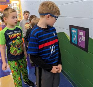 Students reading book page hanging on hallway wall.