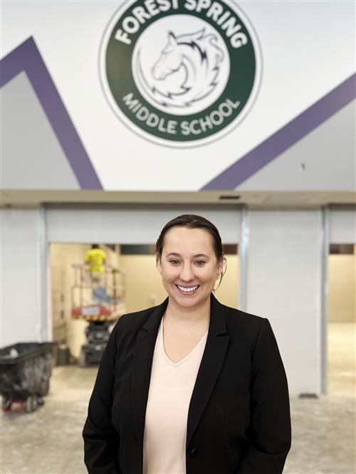 2023-24 FSMS Assistant Principal Lindsey Bales smiling in front of school logo in the new building's unfinished cafeteria