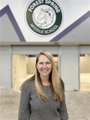 2023-24 FSMS Principal Darcy Sly smiling in front of school logo in the new building's unfinished cafeteria